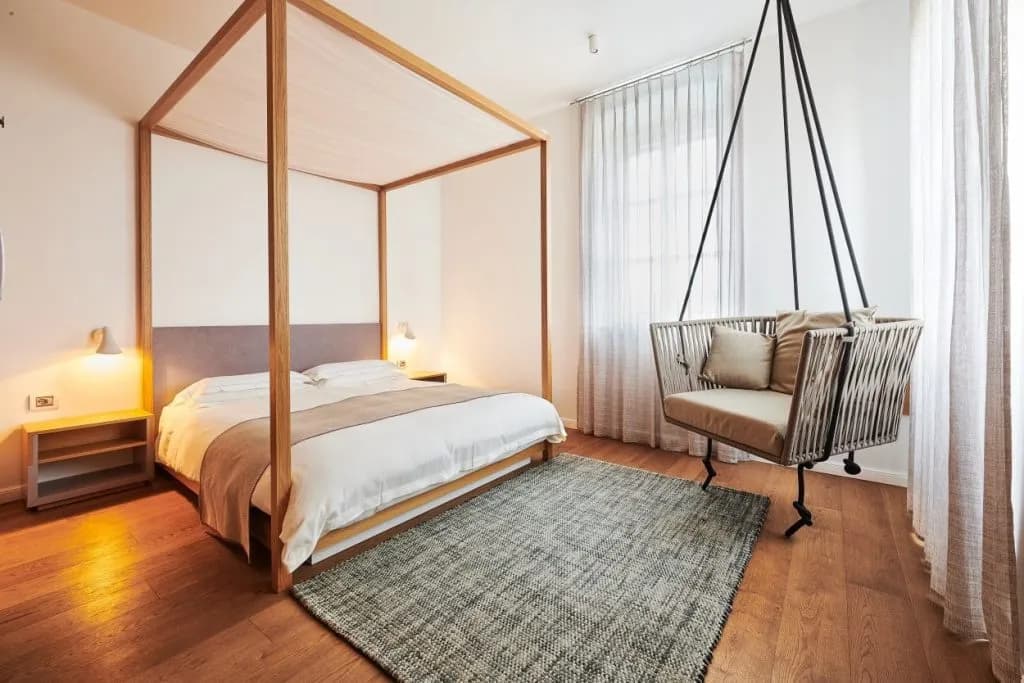 Junior suite bedroom with wooden four-poster bed and hanging woven chair in Manuel Kovača hotel.