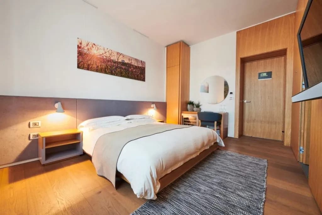Modern double hotel room with wood floors, white bedding, and warm lighting in Gredic Hotel.