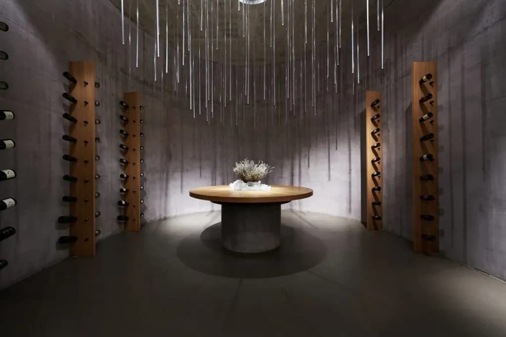 Modern wine cellar with concrete walls, wood racks, and hanging glass light fixture over a central table.