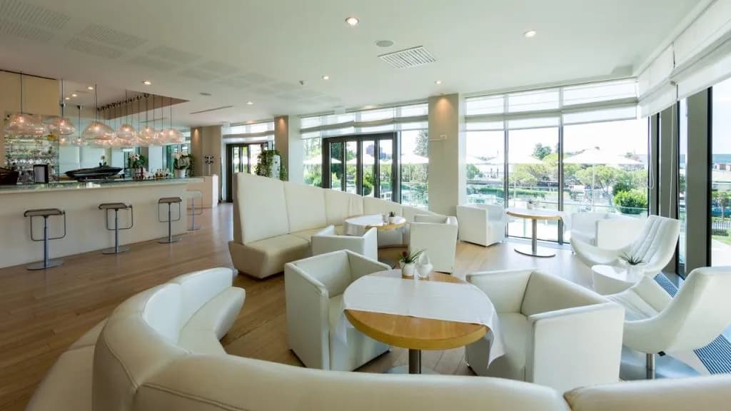 Lobby bar lounge with white modern seating, wood floors, and view of outdoor patio at Hotel Kempinski Palace.