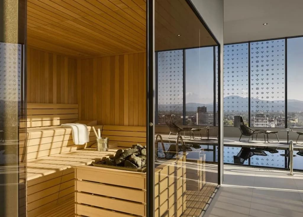 Wooden sauna interior next to an outdoor pool area with city and mountain views