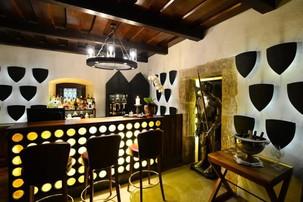Bar with illuminated front, dark wood ceiling, knight statue, and shield decor at Hotel Grad Otočec.