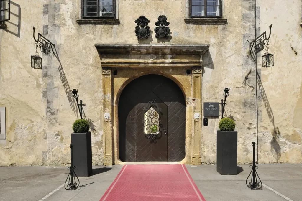 Entrance to Hotel Grad Otočec featuring an arched wooden door, stone facade, and red carpet.