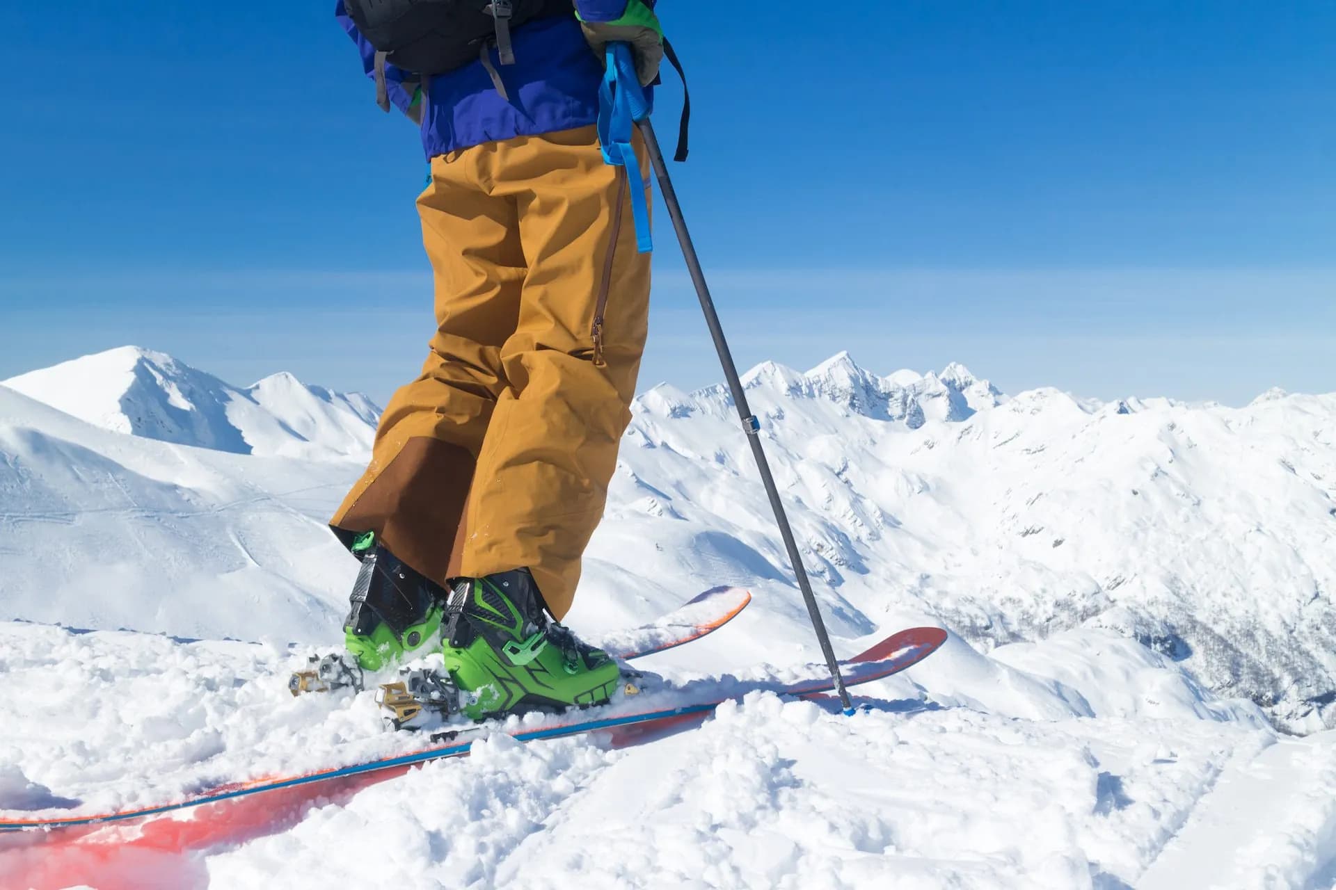 Skier with skis and poles standing on snowy mountain peak under clear blue sky