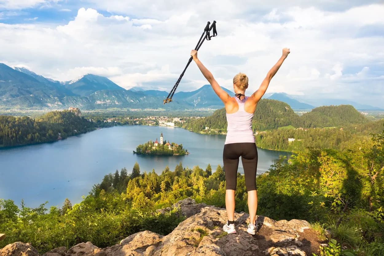 Hiker celebrating on viewpoint overlooking Lake Bled island and Julian Alps in Slovenia