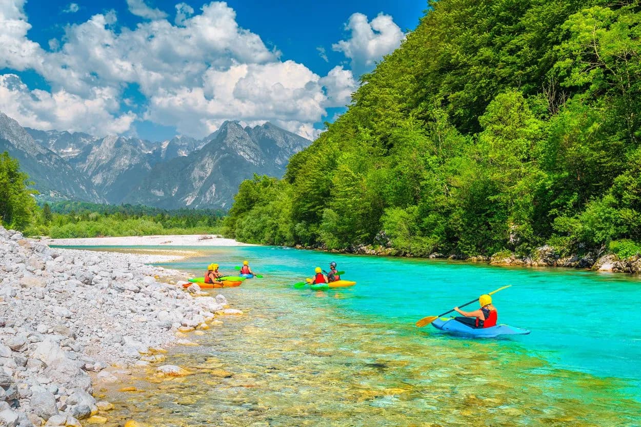 Kayaking on turquoise water of the Sava River with rocky shore and mountains in background.
