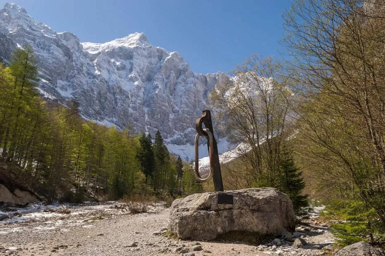 Climbing carabiner sculpture on rock with snow-capped mountains and forest in Vrata Valley