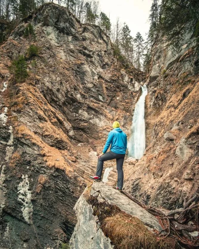 Hiker viewing Martuljek waterfall cascading down steep, rocky gorge walls in the mountains.