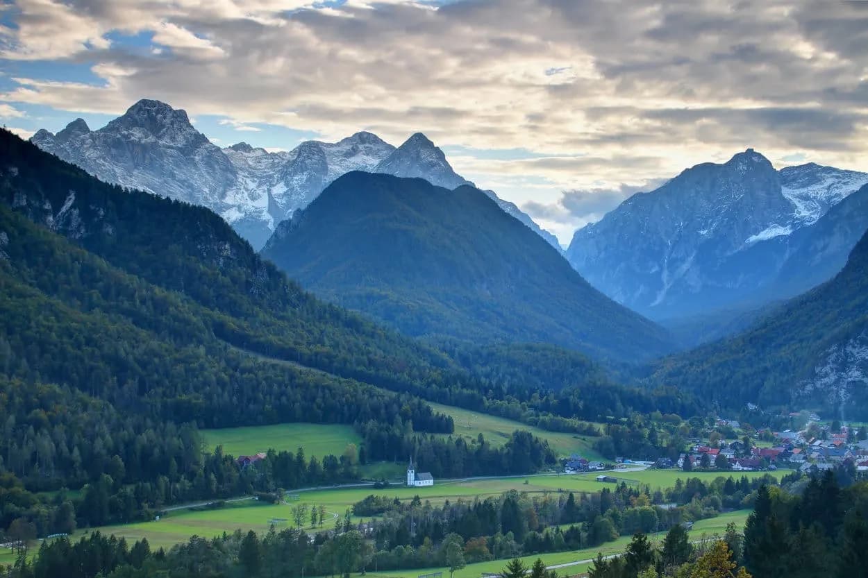 Alpine valley with snow-capped mountains, green meadows, and a small village with a white church.