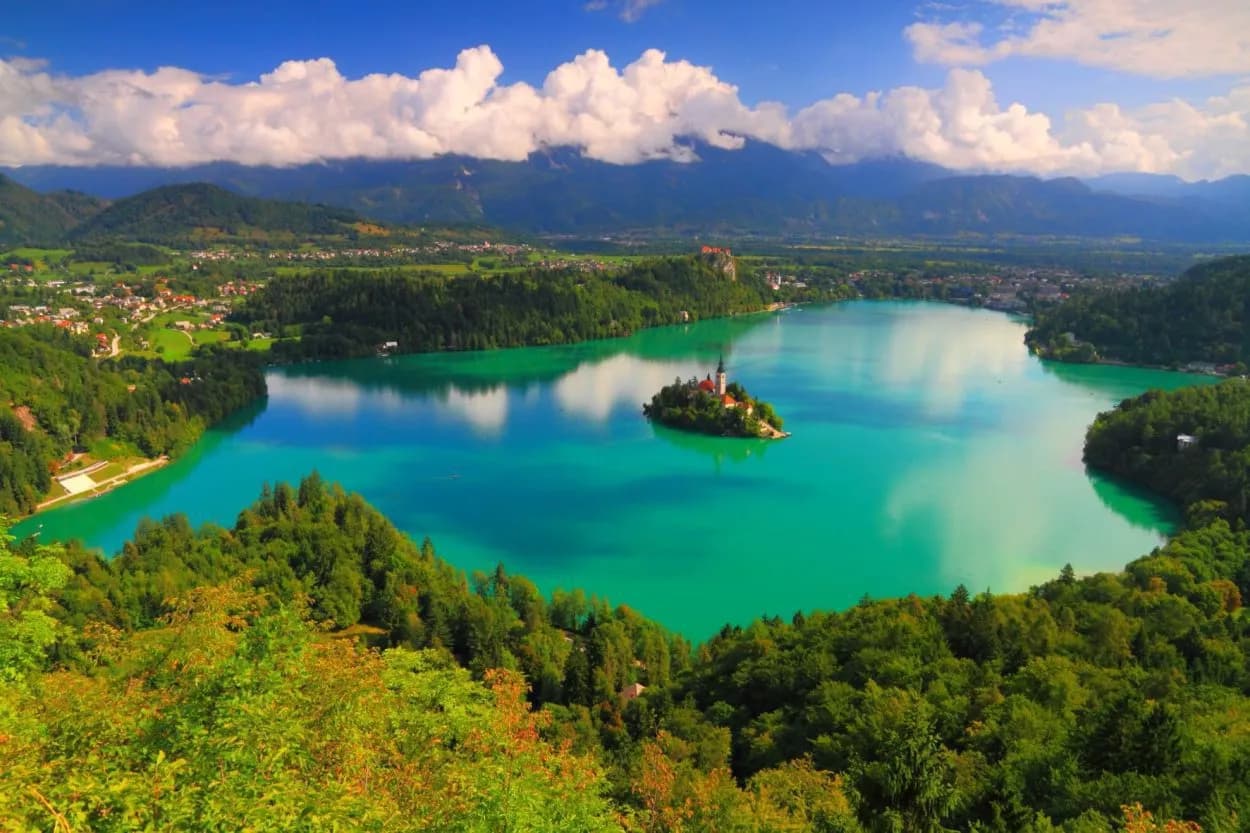 Lake Bled island church surrounded by turquoise water, green forests, and Julian Alps mountains.