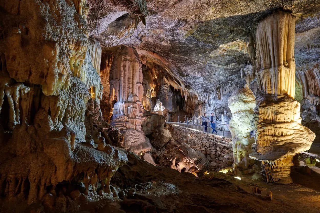 Tourists viewing massive stalactites and stalagmites illuminated inside Postojna Cave.