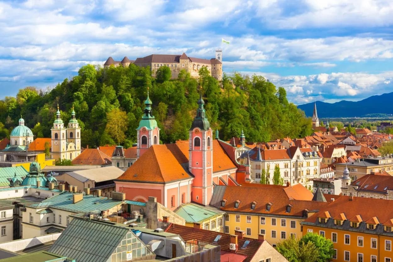 Ljubljana cityscape with castle on green hill, colorful roofs, and mountains in background