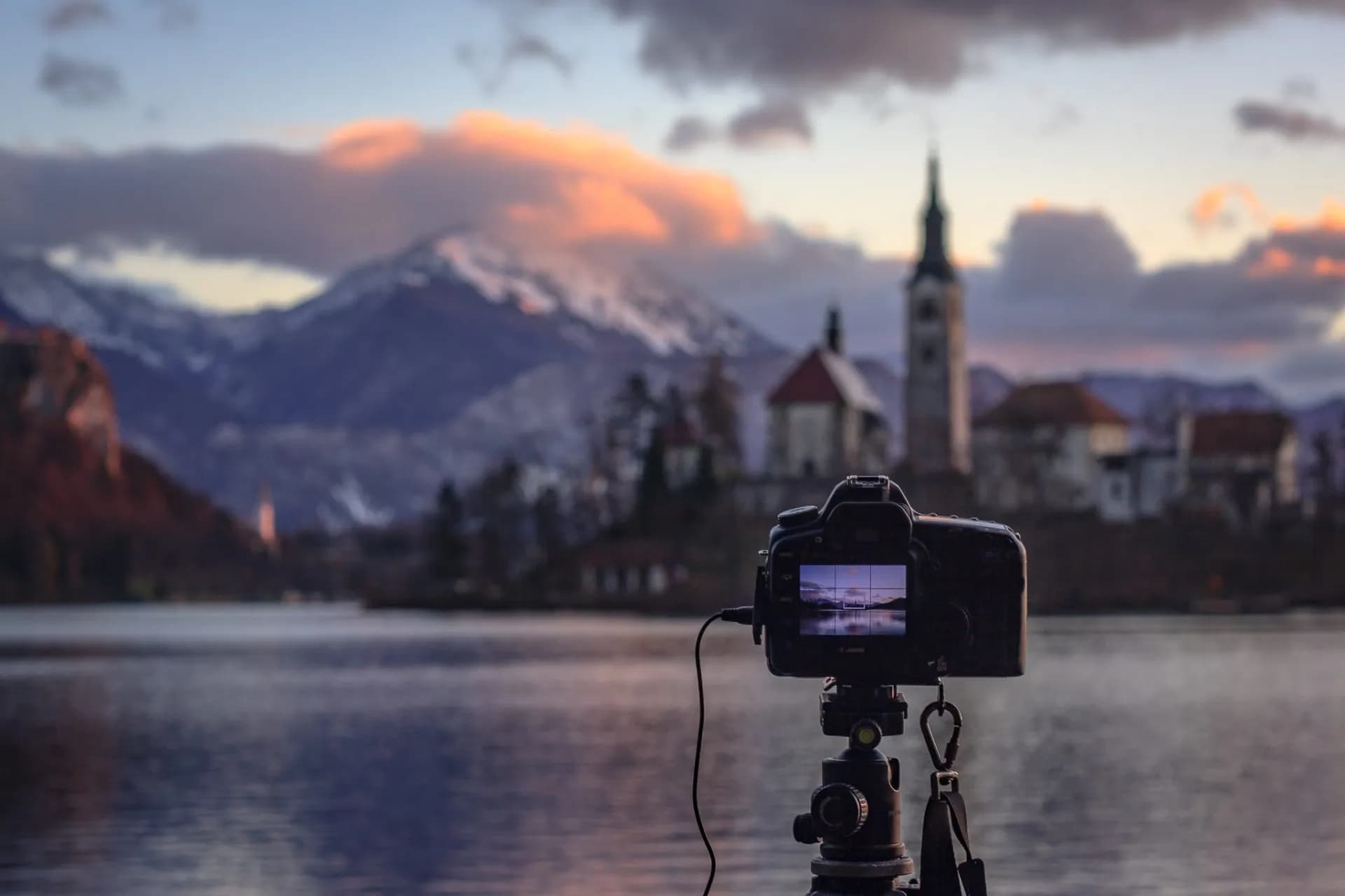 Camera on tripod capturing Lake Bled island church with snowy mountains at sunset