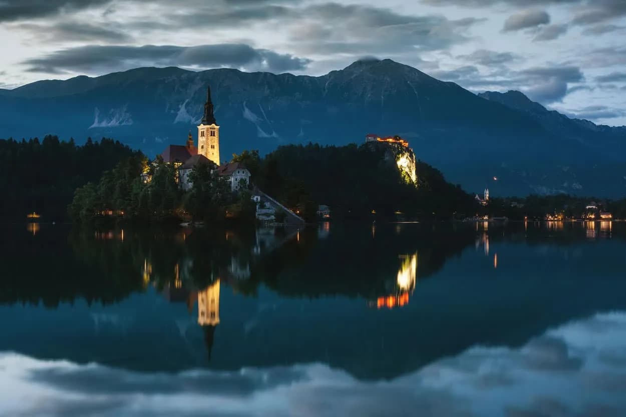 Lake Bled island church and castle illuminated at night with mountain reflection