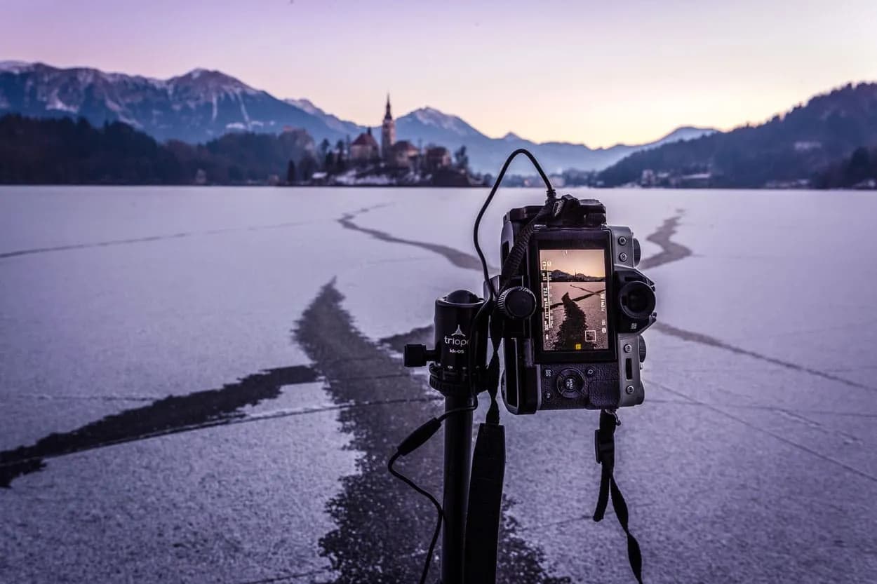 Camera on tripod photographing frozen Lake Bled with island church and mountains