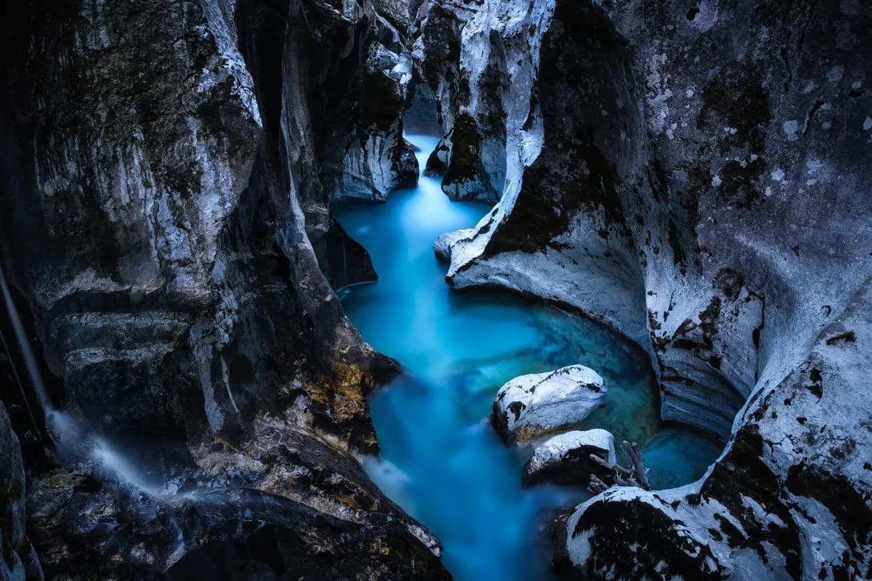 Turquoise river flowing through dark, narrow rock canyon with small waterfall