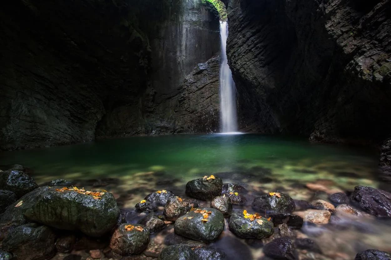 Waterfall cascading into a green pool inside a dark gorge, Slap Kozjak, Slovenia