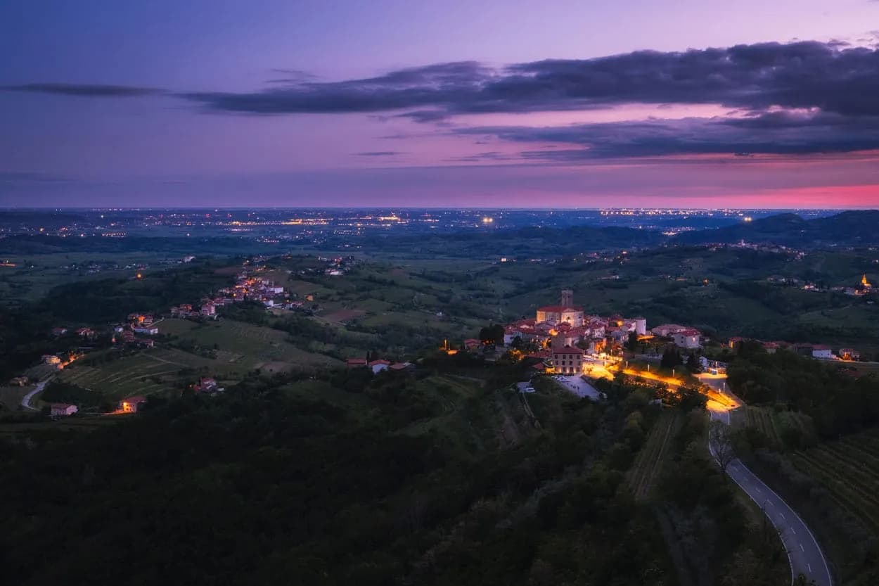 Hilltop village of Šmartno in Brda at twilight with illuminated buildings and rolling green landscape.