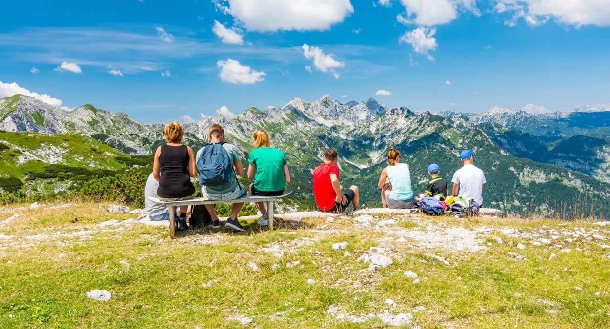 Hikers resting on a bench overlooking green mountains under a blue sky