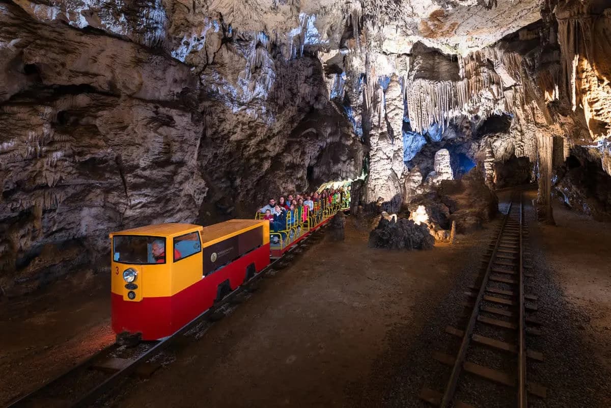Postojna Cave train full of visitors traveling through illuminated cavern with stalactites.