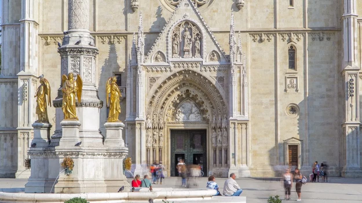 Zagreb Cathedral facade with golden angel statues and blurred people in the square.