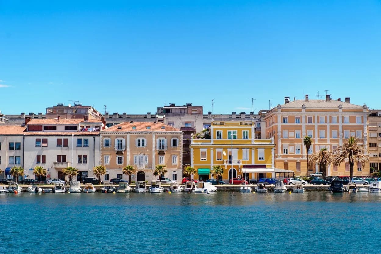 Colorful buildings along the Zadar waterfront with small boats docked on the deep blue sea.