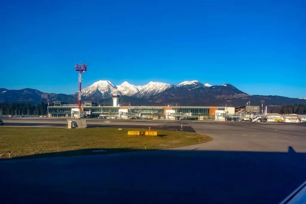 Brnik Airport terminal with snow-capped mountains under a clear blue sky