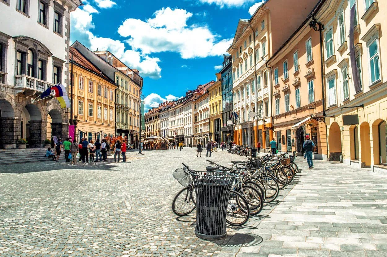 Cobblestone square in Old Town Ljubljana with historic buildings and parked bicycles under a blue sky.
