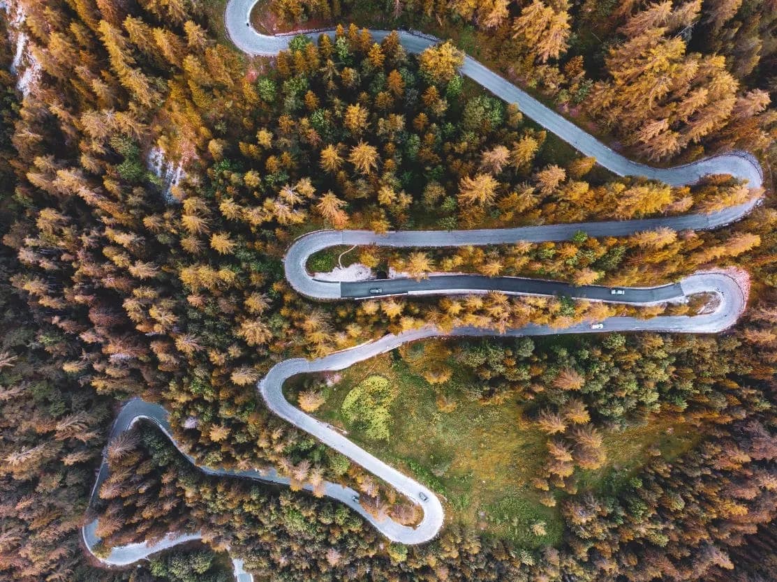 Aerial view of winding mountain road with switchbacks through autumn forest foliage.