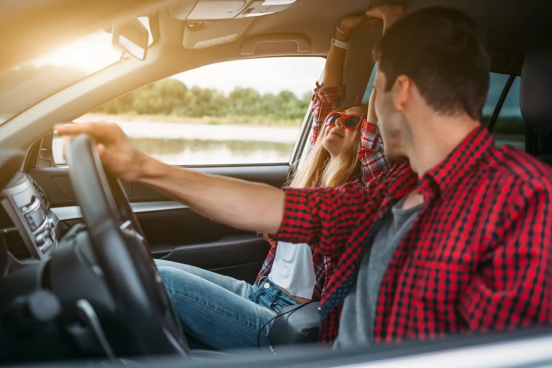 Couple enjoying self-drive holiday inside car with water and trees visible outside.