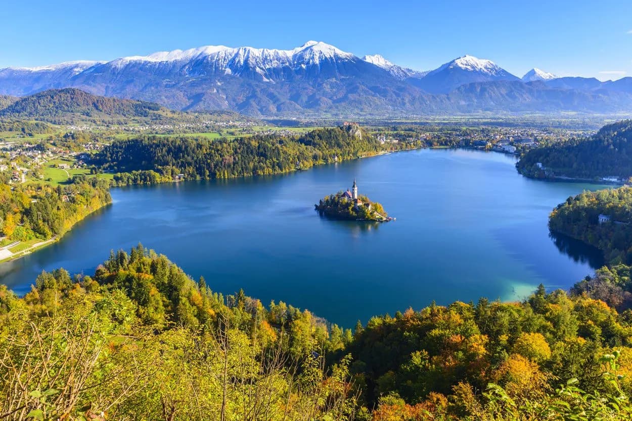 Lake Bled island church with Julian Alps snow-capped mountains and autumn foliage