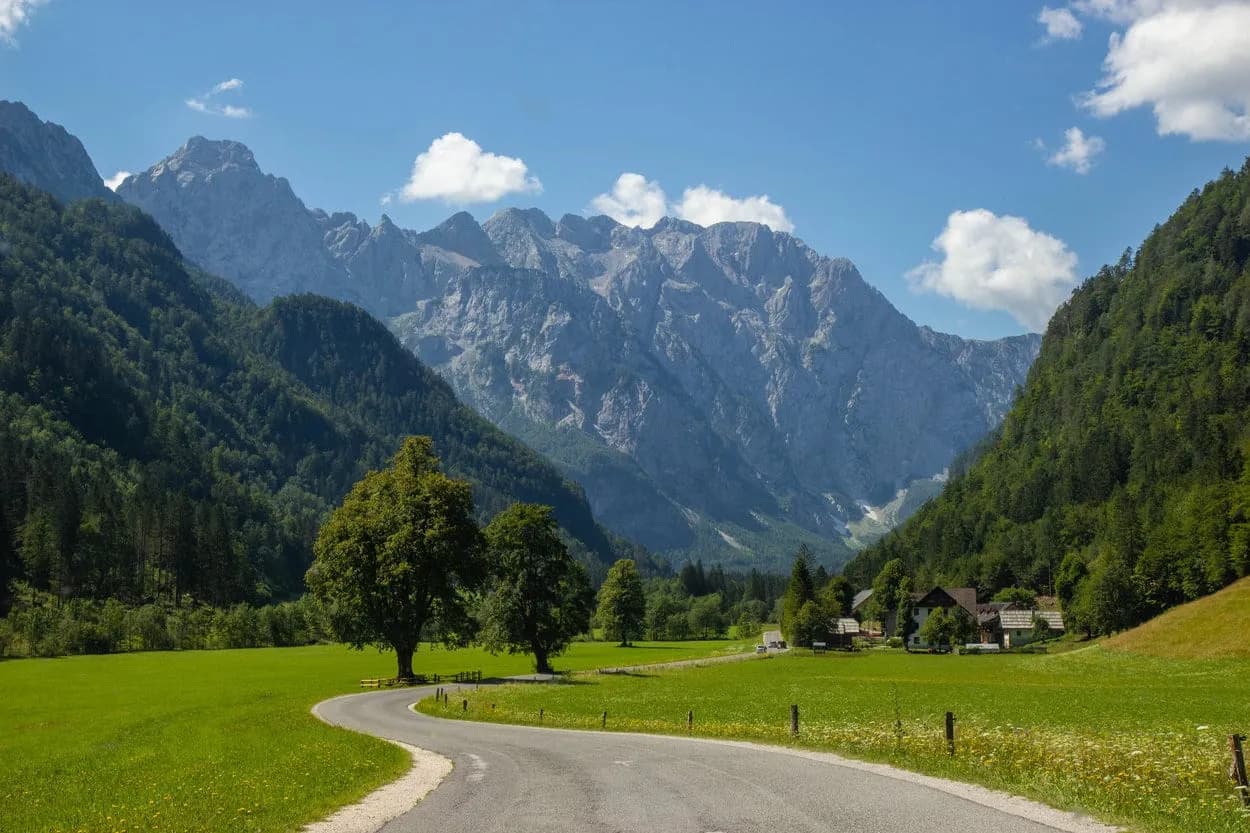 Winding road through green valley toward rocky mountains in Logar Valley, Slovenia