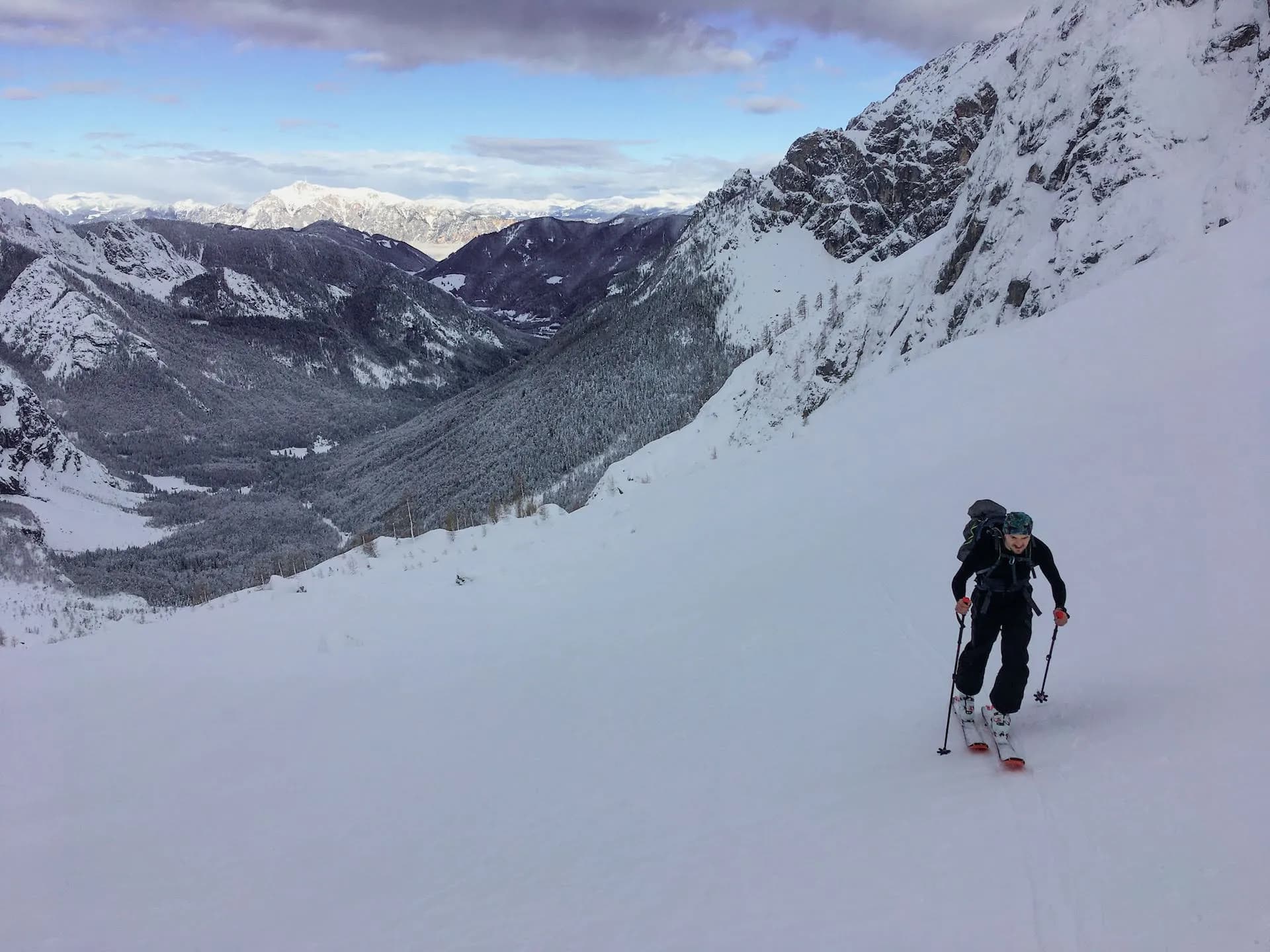 Ski touring uphill on deep snow slope with snowy mountains and valley below