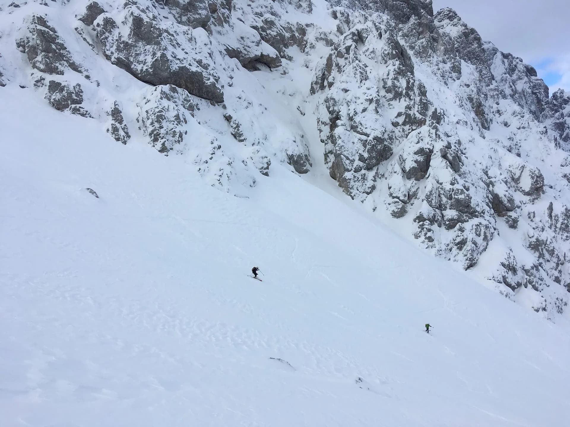 Skiing down a steep, snow-covered mountain face with rocky outcrops above.