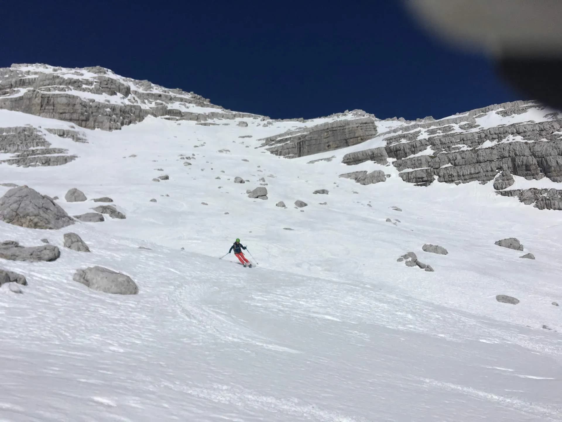Skiing down a snowy slope with exposed rock faces under a dark blue sky on Mojstrovka.