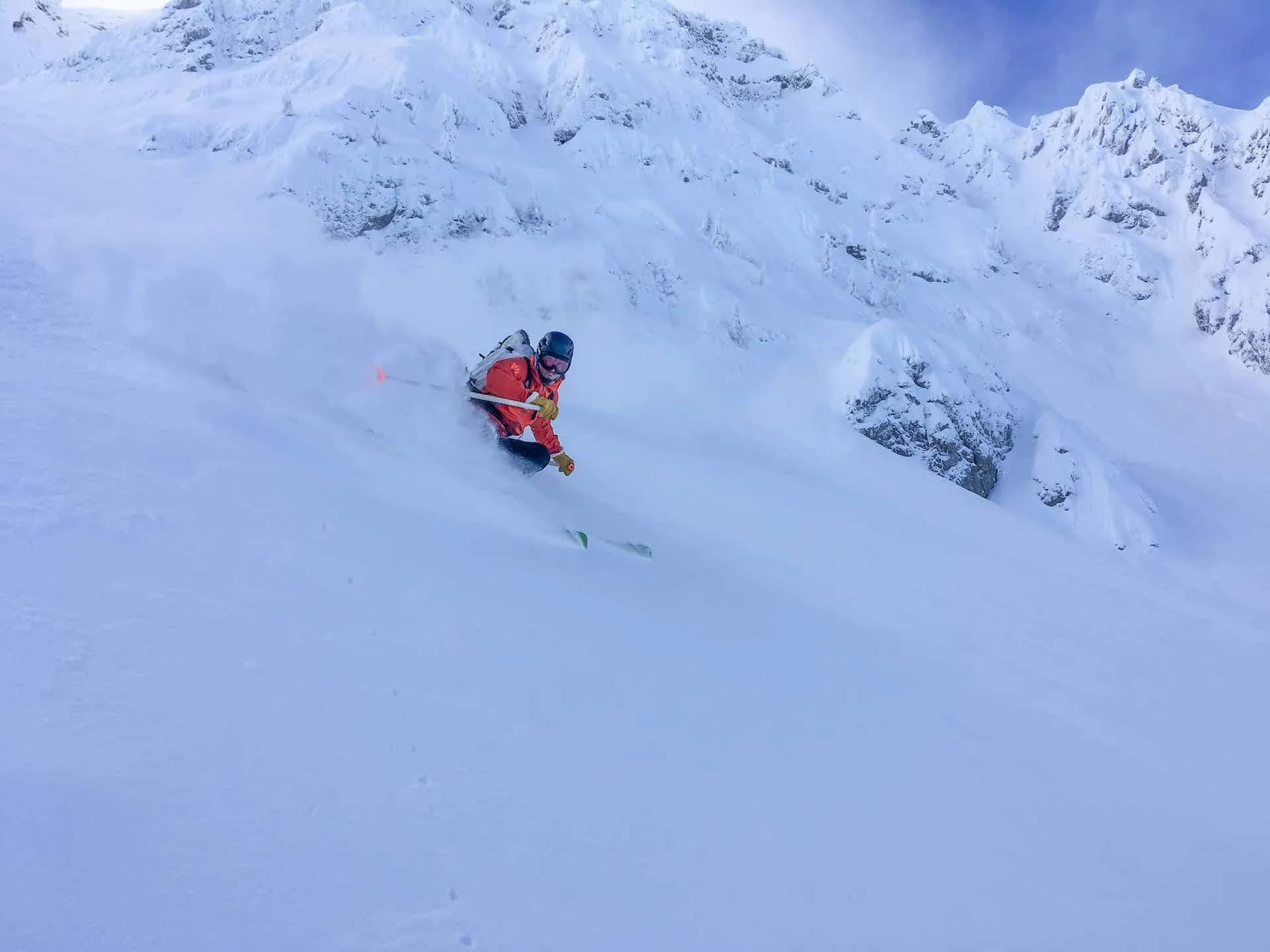 Powder skiing above Zelenica on steep, snow-covered alpine terrain under a blue sky.
