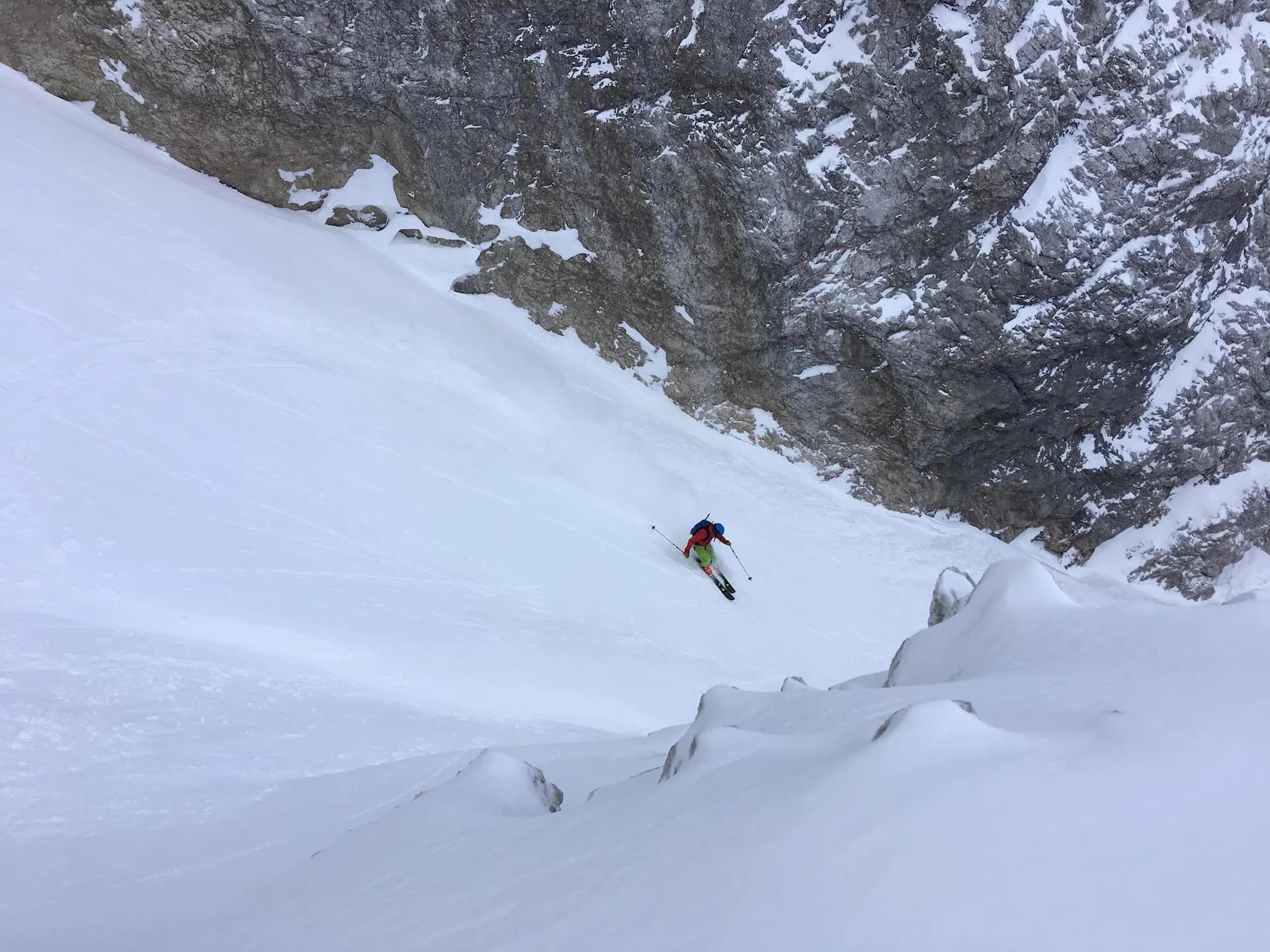 Skiing down a steep, snowy slope next to a massive gray rock face in Jalovcev Ozebnik.
