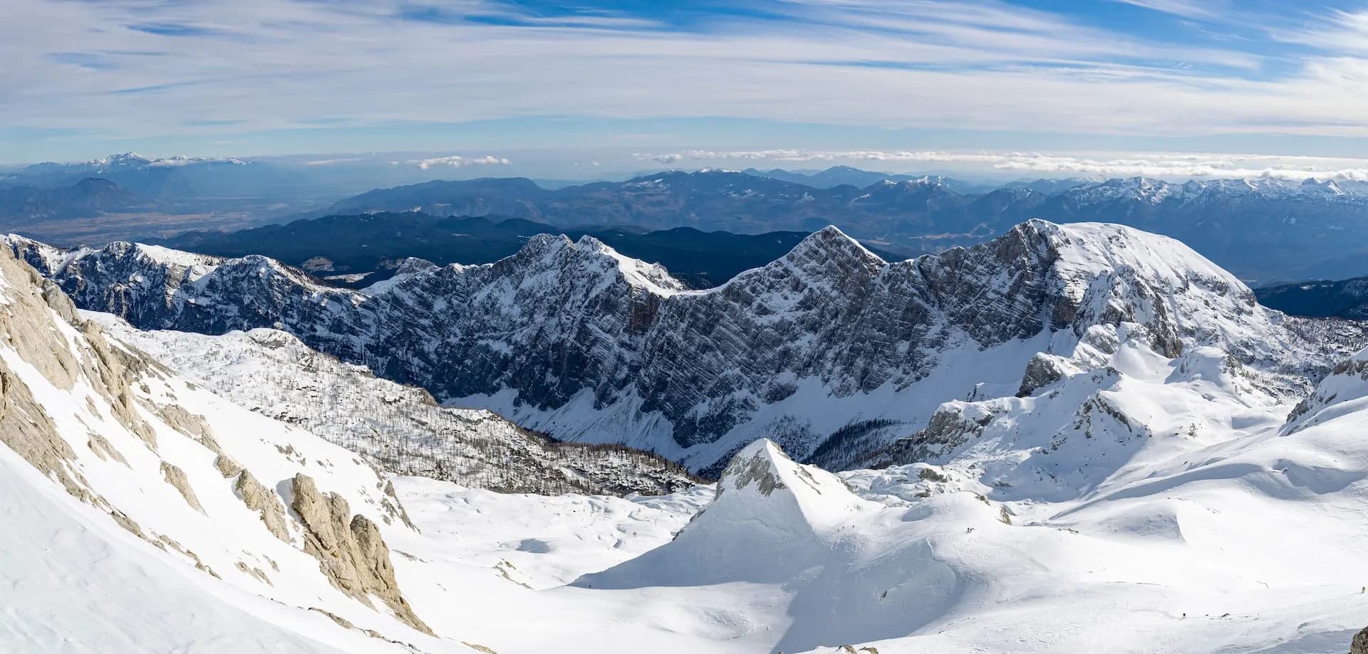 View from Kredarica in winter showing snow-covered Julian Alps peaks under a blue sky.