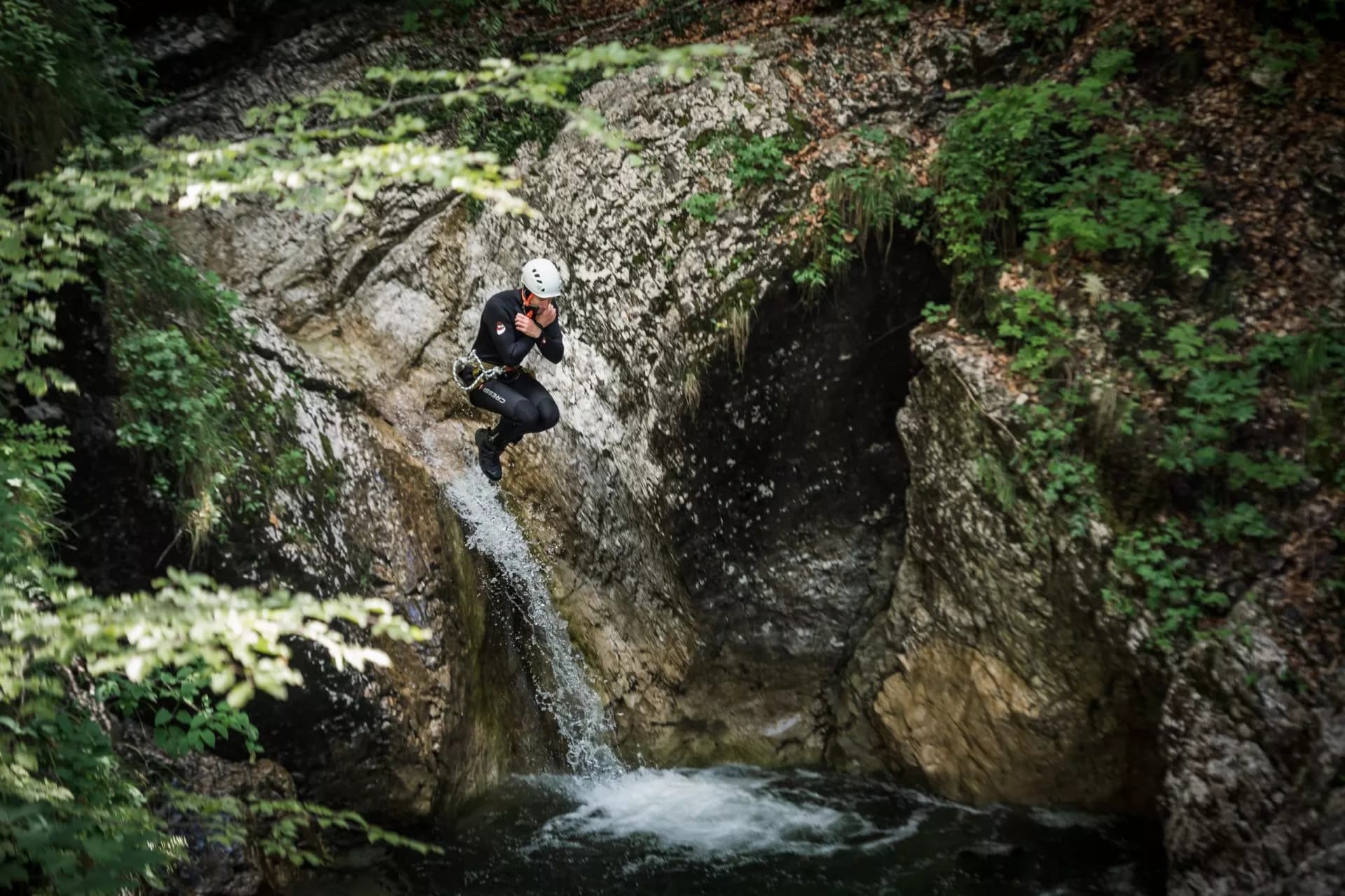 Canyoning jump into pool from waterfall between mossy canyon walls in Slovenia