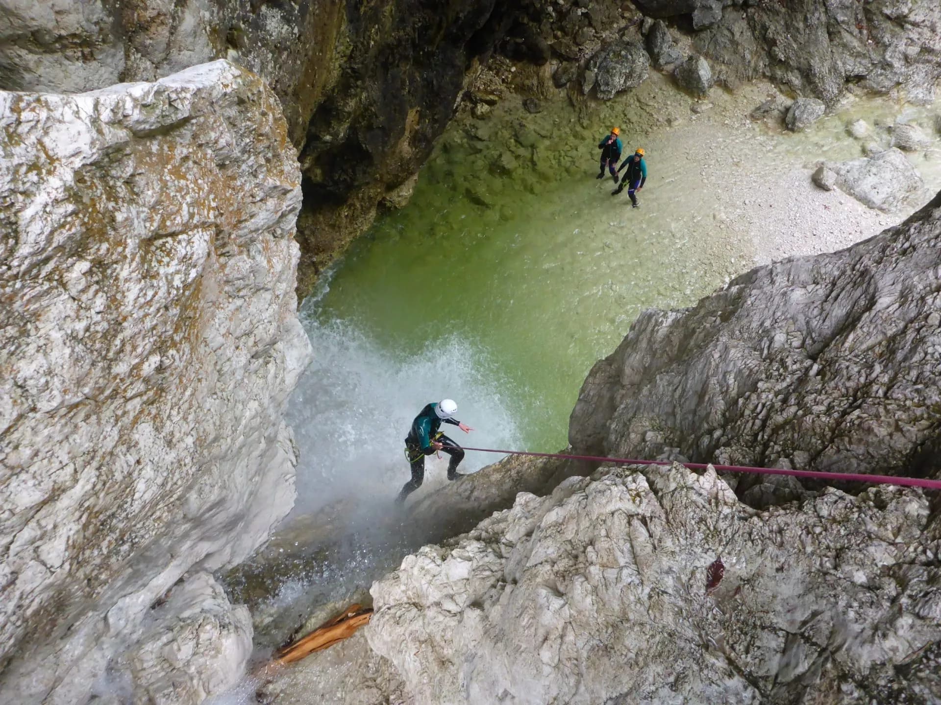Abseiling during canyoning in Slovenia, descending a waterfall into a green pool.