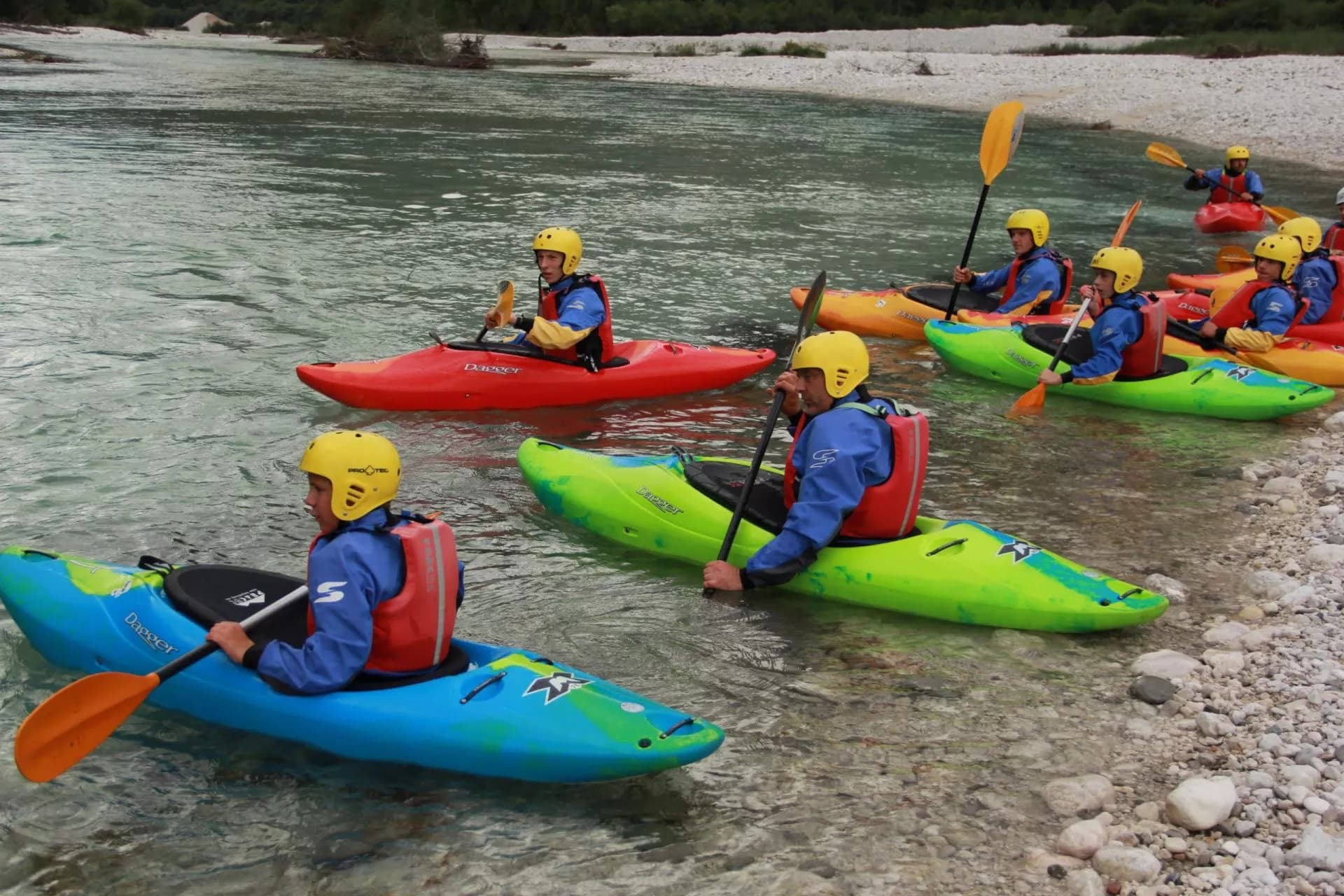 Kayaking group in colorful boats on shallow river near rocky shore, Slovenian Rivers.