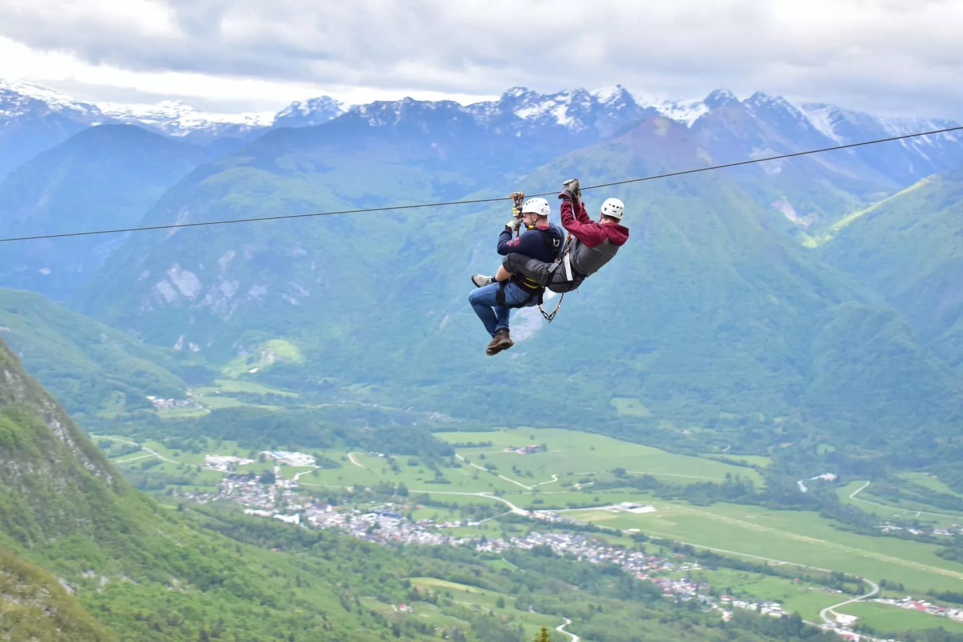 Ziplining over Soca Valley with green slopes and snow-capped mountains in background