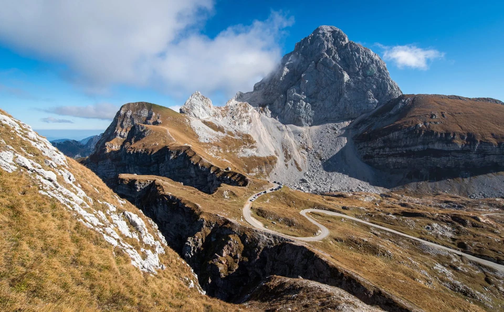 Winding mountain road scaling steep slopes near Mangart peak under blue sky