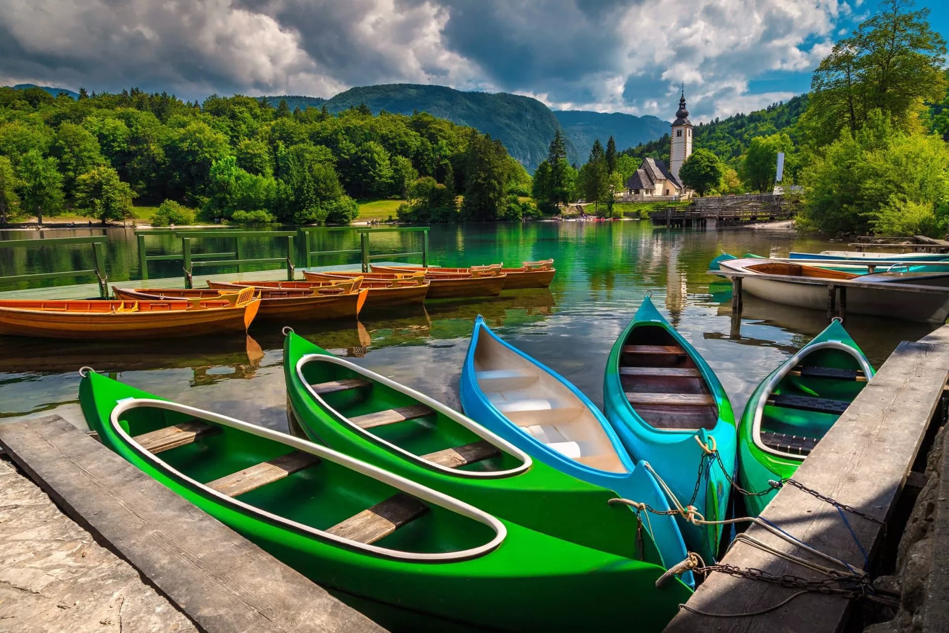 Canoes and wooden boats docked on Lake Bohinj with a church tower and green mountains.