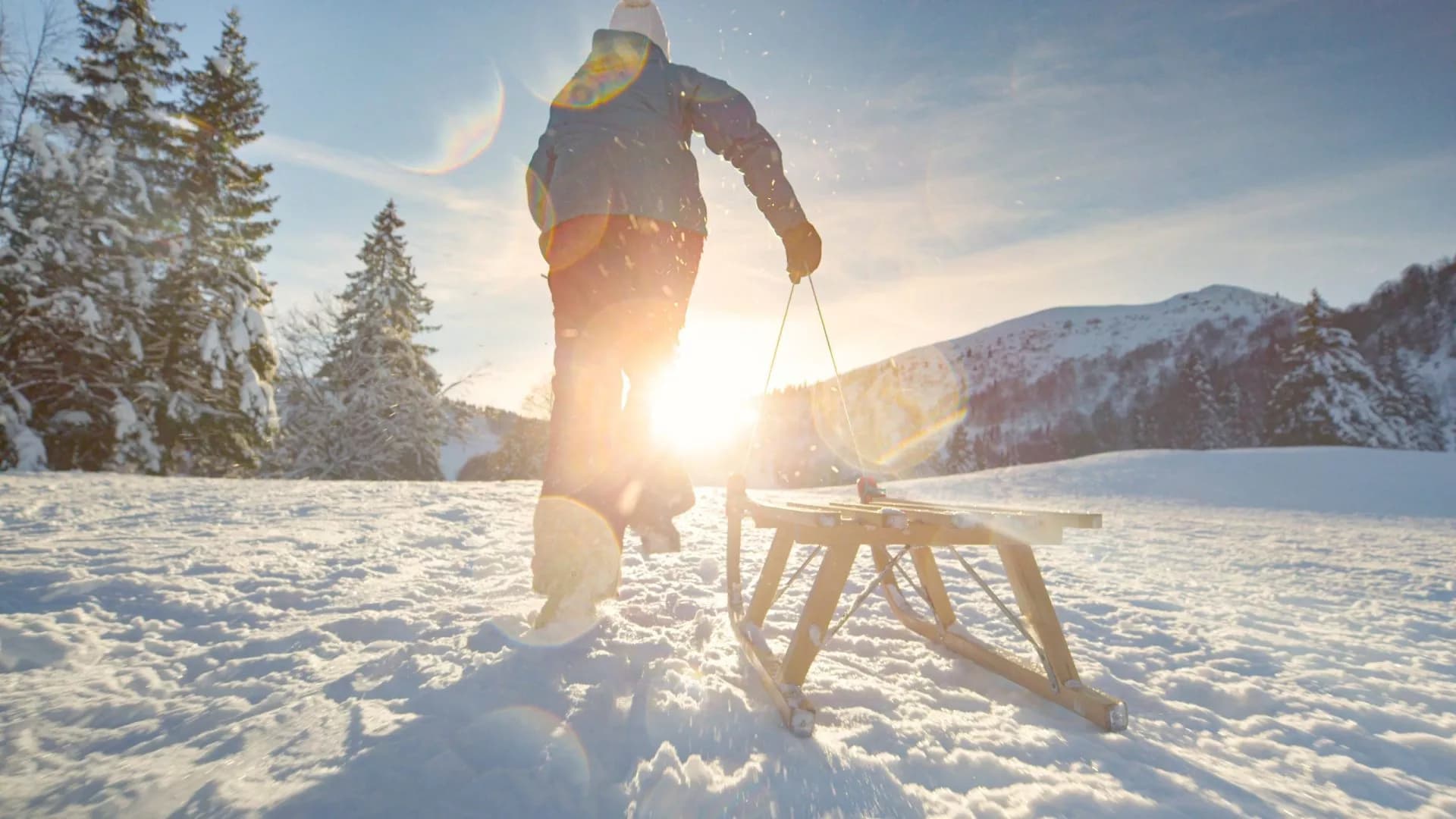 Person pulling wooden sled through deep snow on sunny winter mountain slope