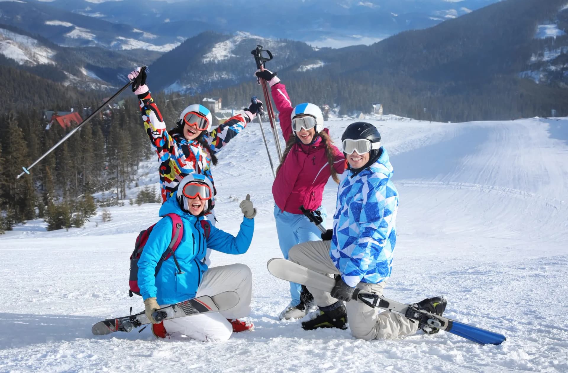 Four skiers posing happily on a snowy mountain slope with forested hills in the background.