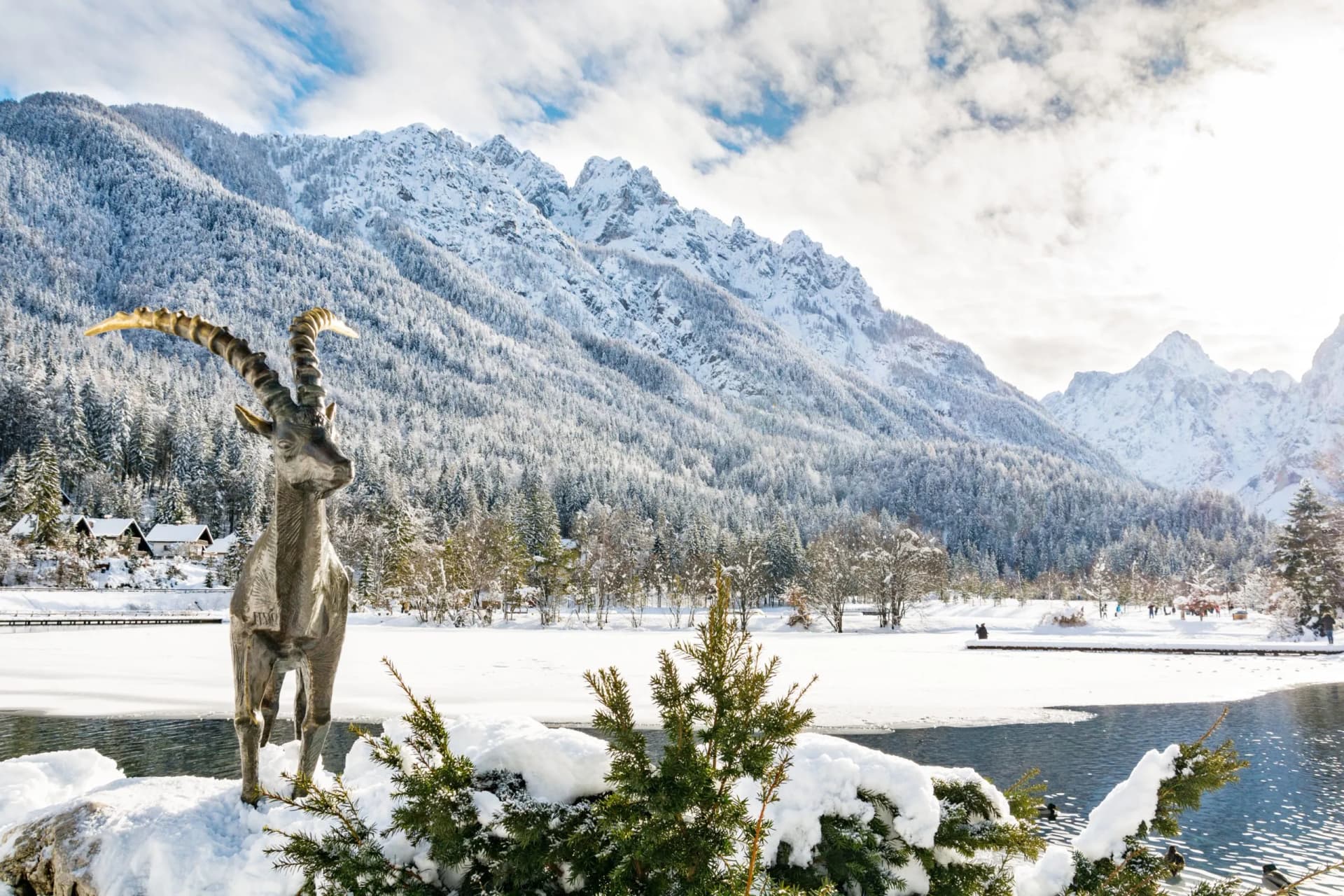 Ibex statue by partially frozen Lake Jasna with snow-covered mountains in winter.