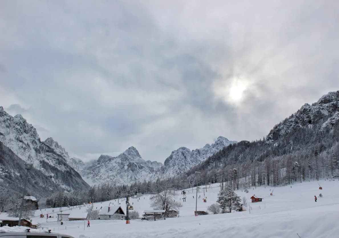 Skiers on snow slopes at Kranjska Gora family ski area with snow-covered mountains.