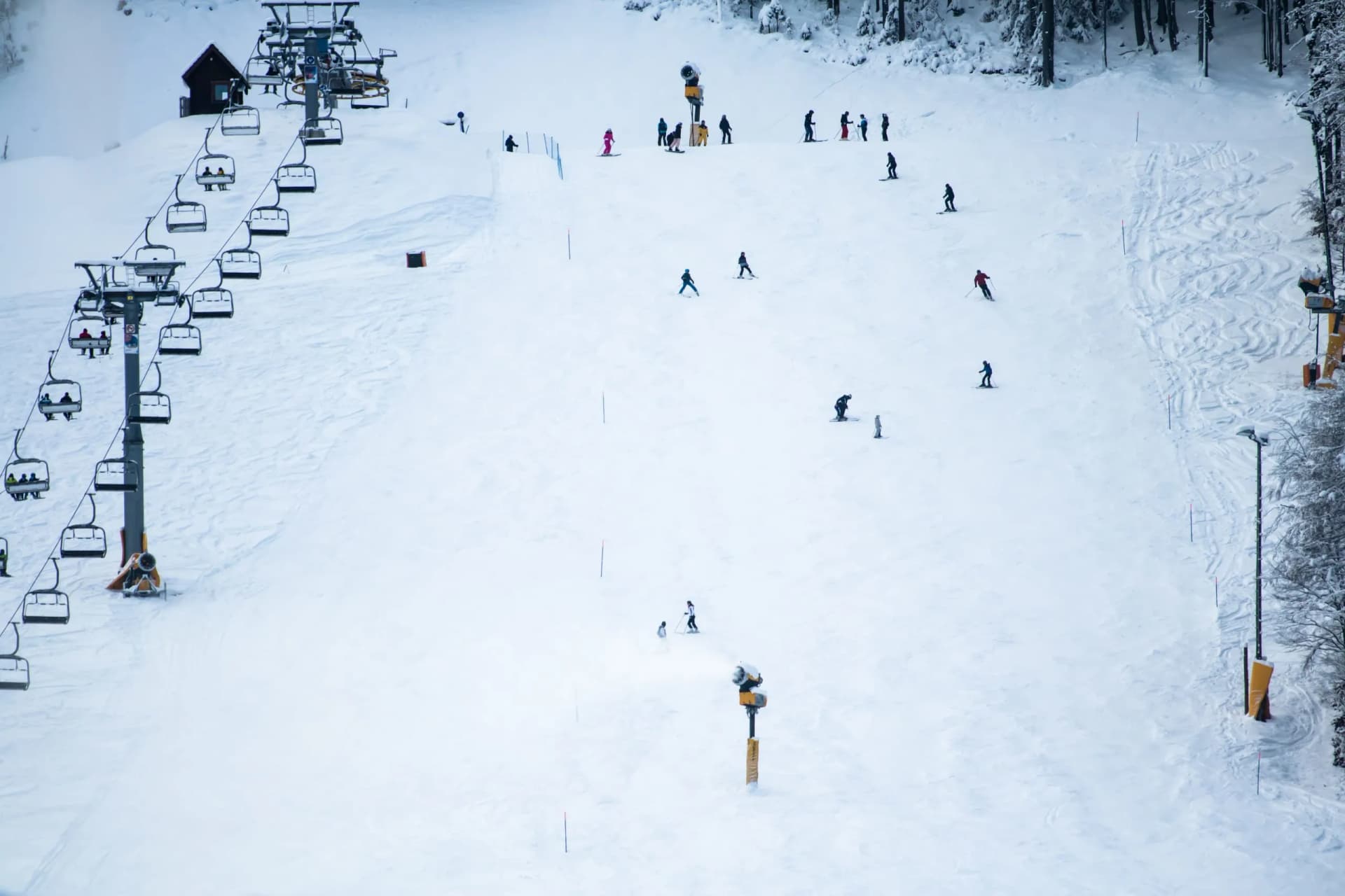 Skiers descending a snowy slope with a chairlift and snow guns at Kranjska Gora.