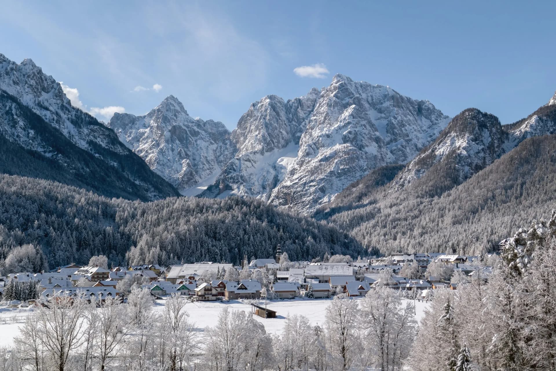 Snowy alpine village nestled below massive, snow-covered mountains under a clear blue sky in Kranjska Gora.